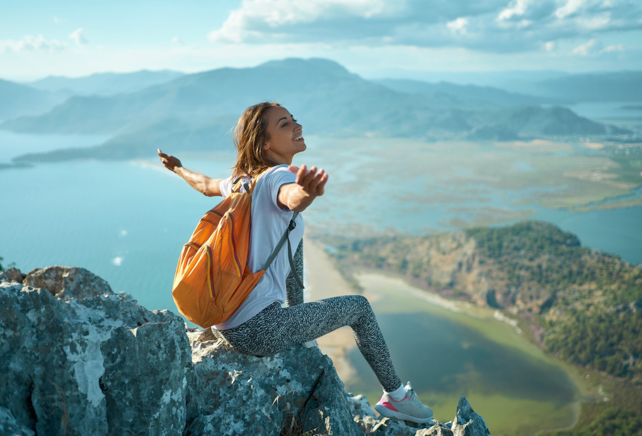 Mujer joven festeja su viaje en la cima de la montaña